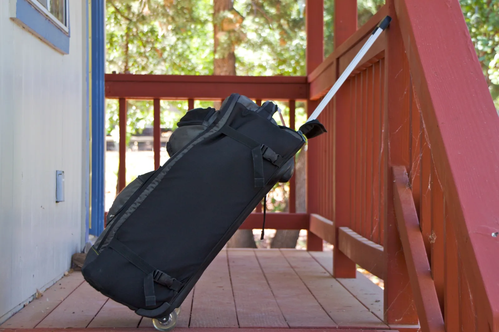 Black wheeled travel bag resting on a cabin porch before a trip