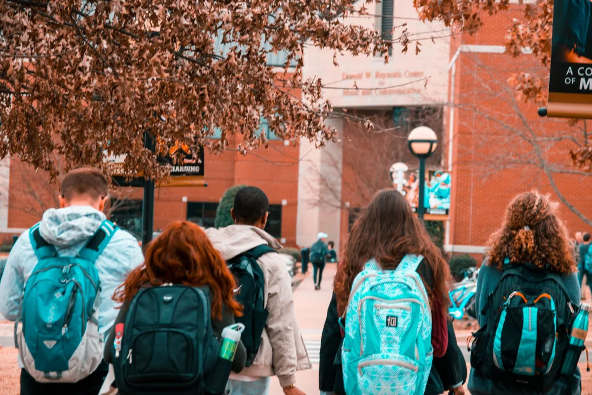 Students wearing daypack backpacks on an autumn campus walk
