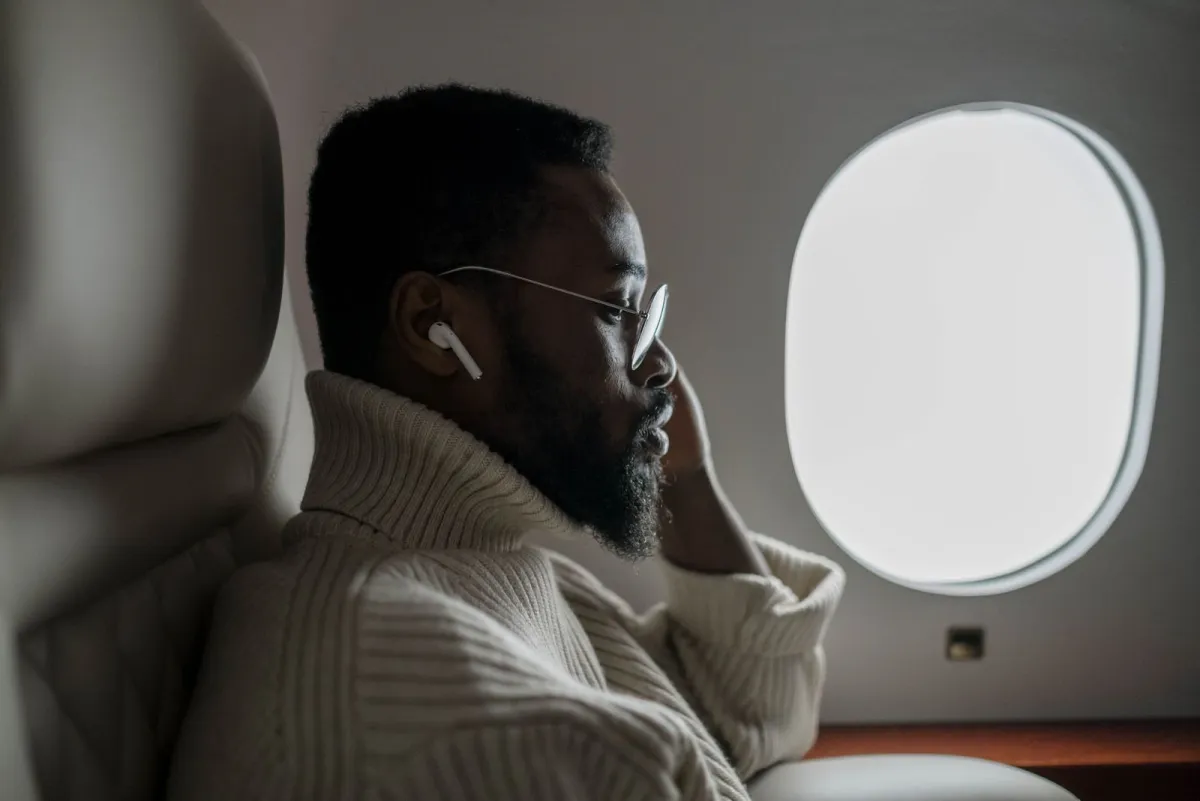 Passenger in a window seat wearing wireless earbuds during the flight