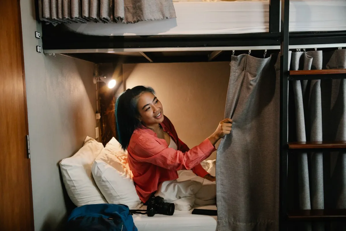 Traveler sitting in a hostel bunk with a backpack on the bed