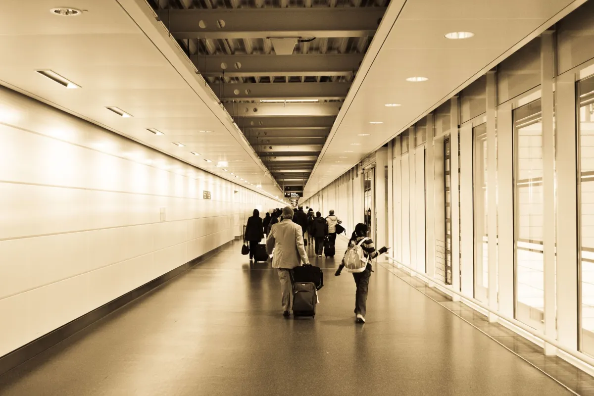 Travelers walking an airport corridor with rolling suitcases and a backpack
