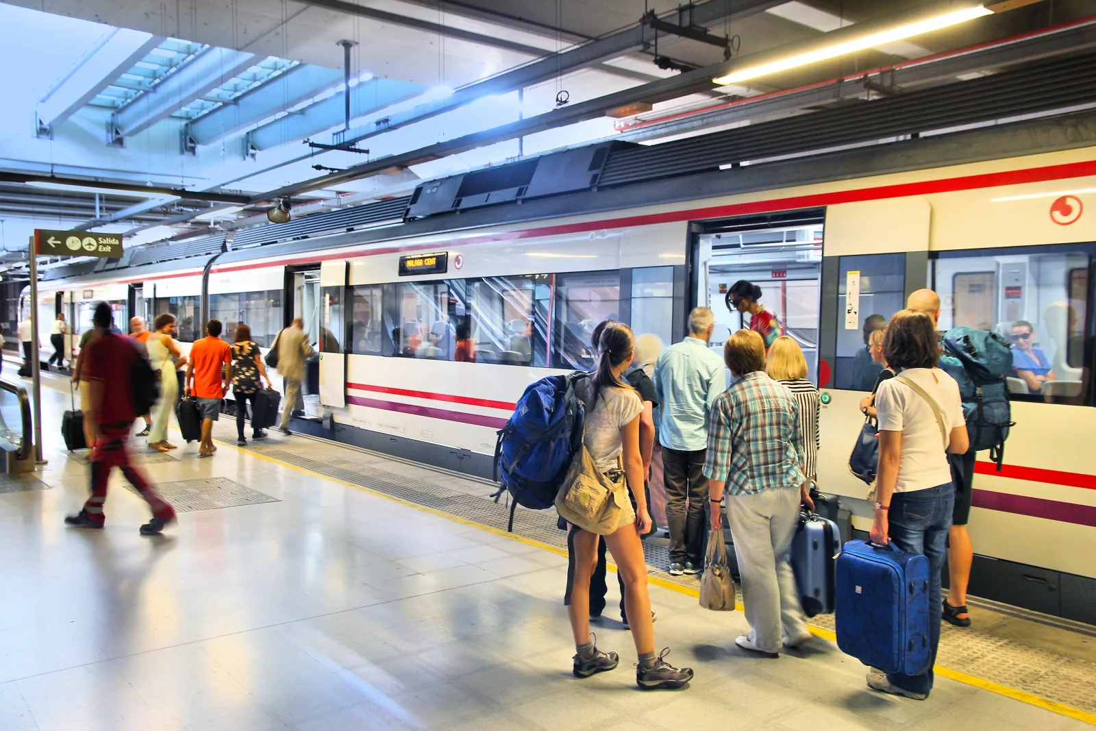 Travelers boarding an airport train with backpacks and wheeled suitcases