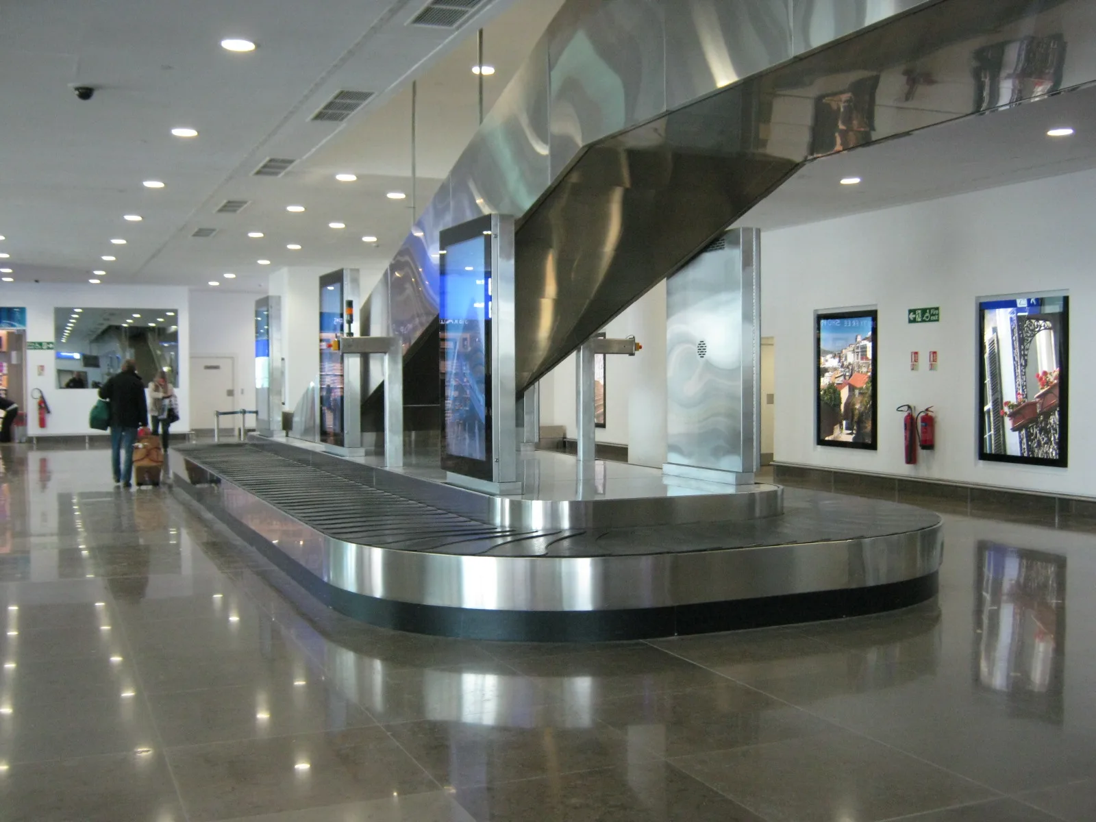 Traveler beside a wheeled bag in a quiet airport baggage hall