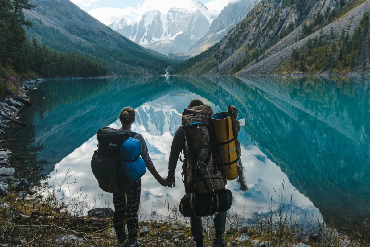 Two hikers with loaded trekking backpacks standing at an alpine lake