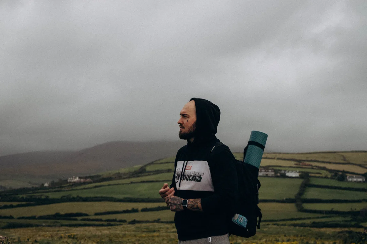 Hiker with a backpack looking across green fields under a cloudy sky
