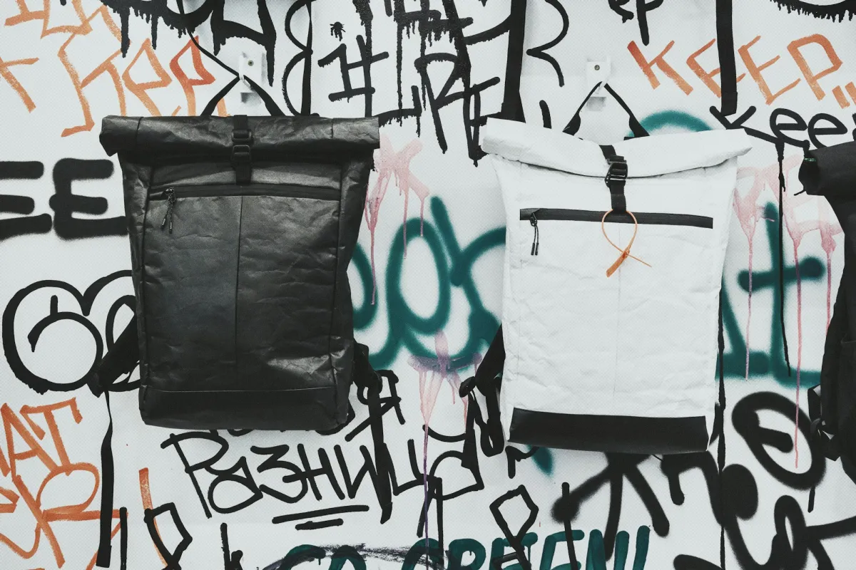 Black and white roll-top backpacks hanging on a graffiti-covered wall