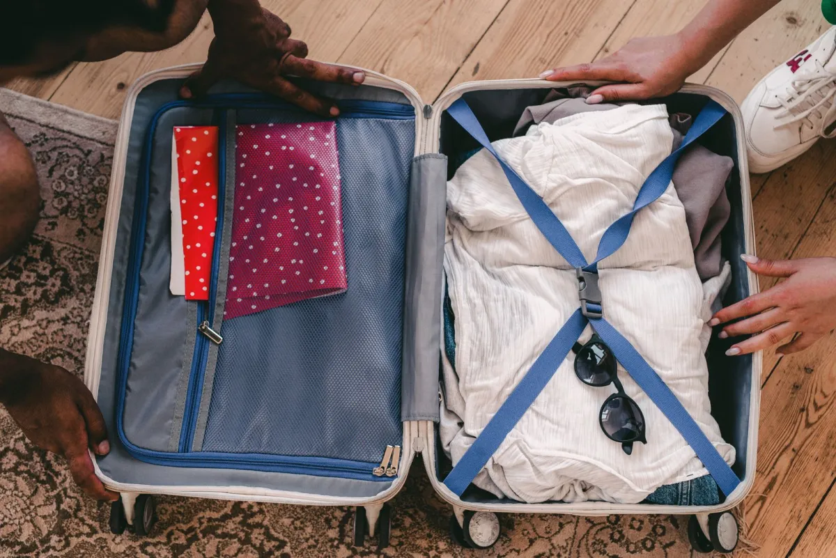 Open suitcase on a rug with clothes held flat under crossed compression straps