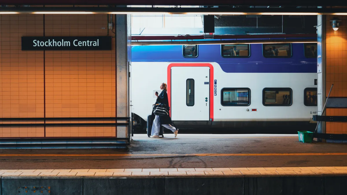 Traveler pulling a suitcase and carrying a tote beside a train at Stockholm Central.