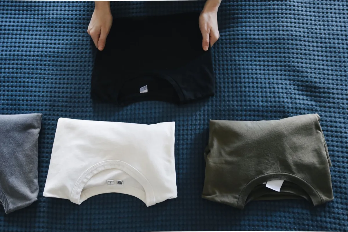 Hands smoothing T-shirts folded into neat flat rectangles on a blue waffle bedspread