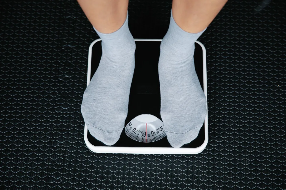 Feet in gray socks standing on an analog bathroom scale, seen from above