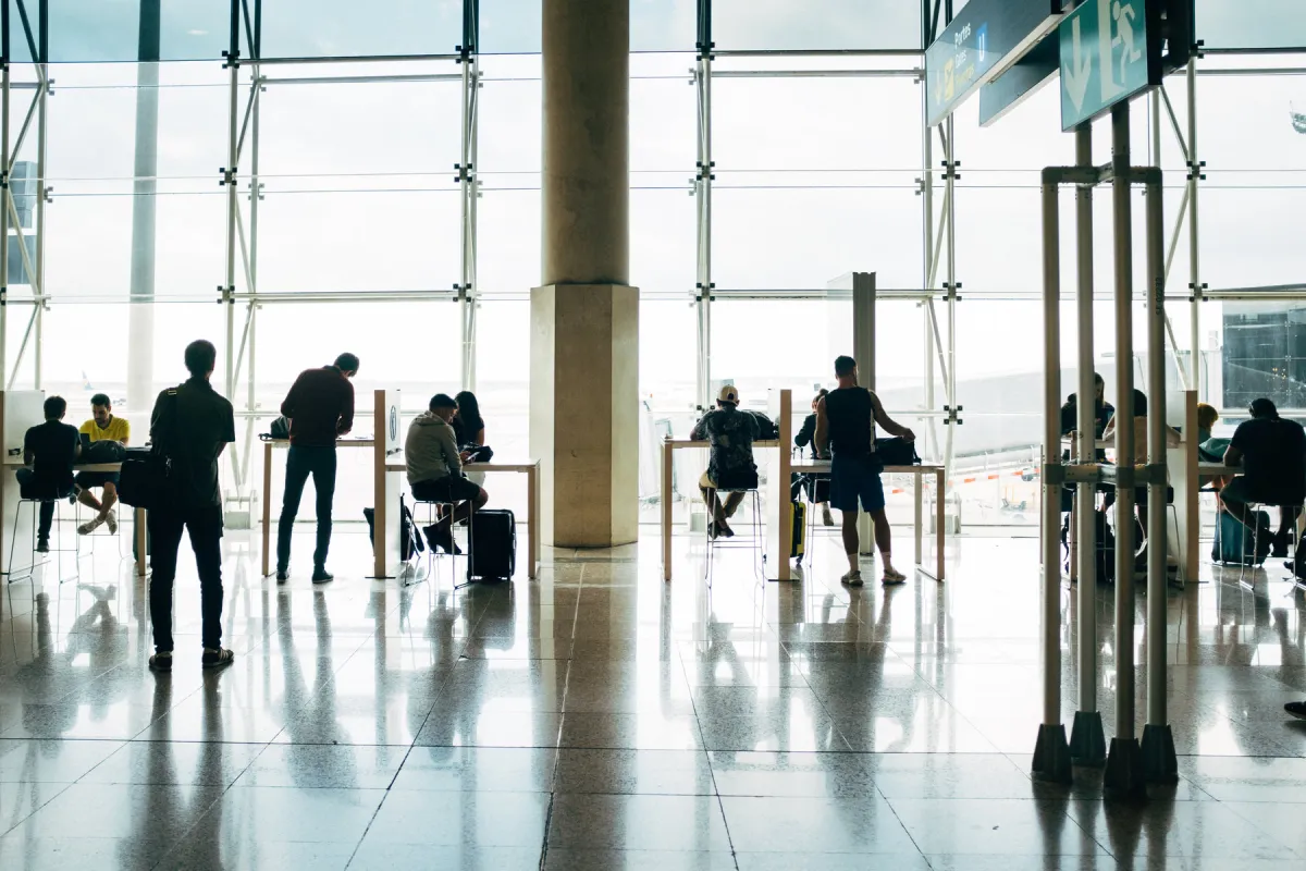 Travelers with carry-on suitcases waiting at a sunlit airport gate lounge