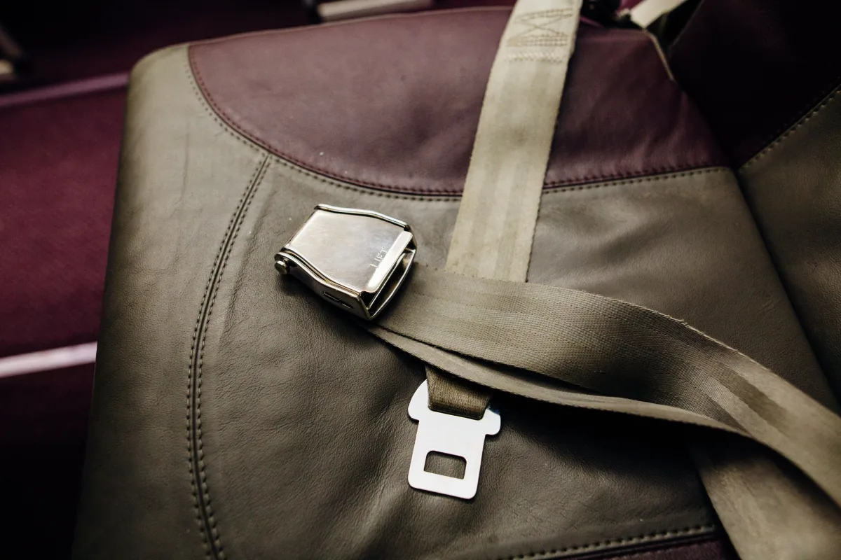 Unfastened airplane seat belt lying across a gray leather cabin seat