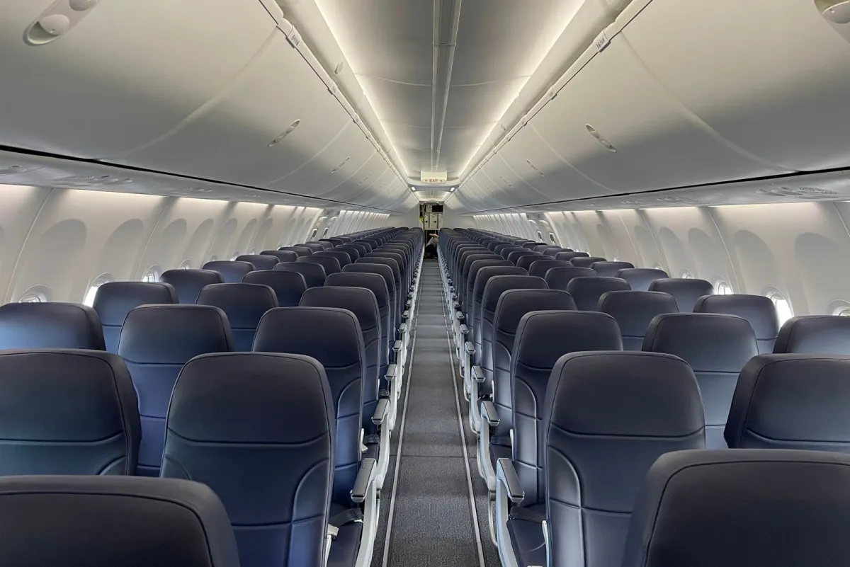 Empty airplane cabin with rows of dark blue seats and closed overhead bins along a center aisle