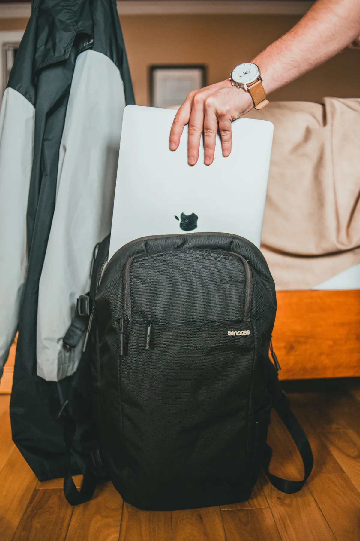 Hand holding a laptop partly inside an open black backpack.