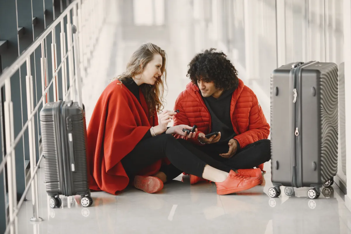 Two people sitting on the floor between upright suitcases.
